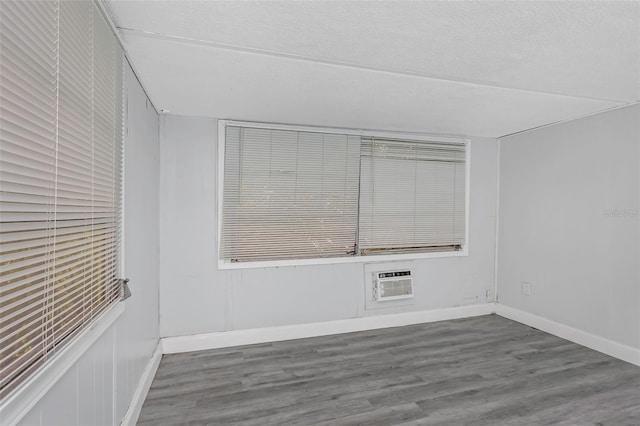 empty room with a wall unit AC, a textured ceiling, baseboards, and wood finished floors