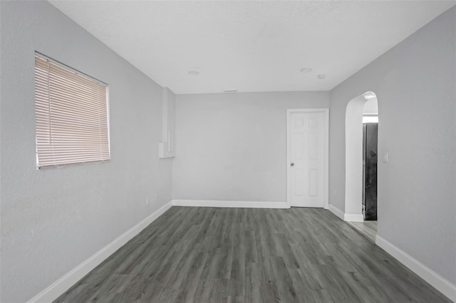 unfurnished room with arched walkways, baseboards, and wood finished floors