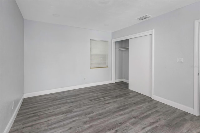 unfurnished bedroom with a closet, wood finished floors, visible vents, and baseboards