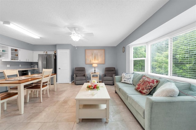 living room with a textured ceiling, ceiling fan, and light tile patterned floors