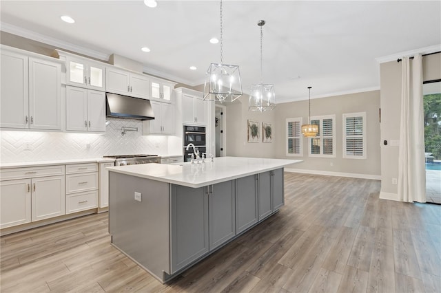 kitchen with white cabinetry, extractor fan, decorative light fixtures, a center island with sink, and ornamental molding