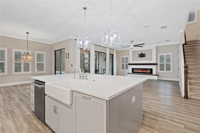 kitchen with a kitchen island with sink, light hardwood / wood-style flooring, ceiling fan, a fireplace, and decorative light fixtures