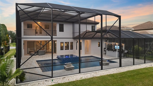 back house at dusk featuring a patio, a balcony, a lanai, and a pool with hot tub