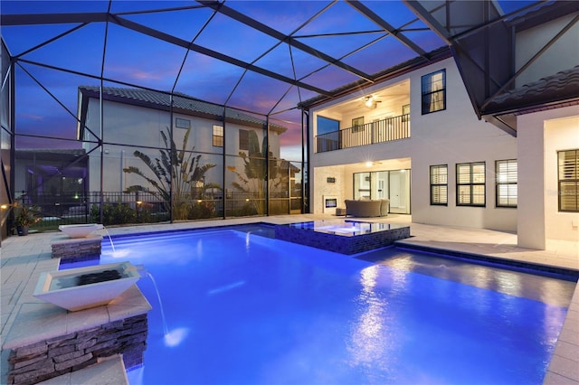 pool at dusk featuring an in ground hot tub, a lanai, pool water feature, ceiling fan, and a patio