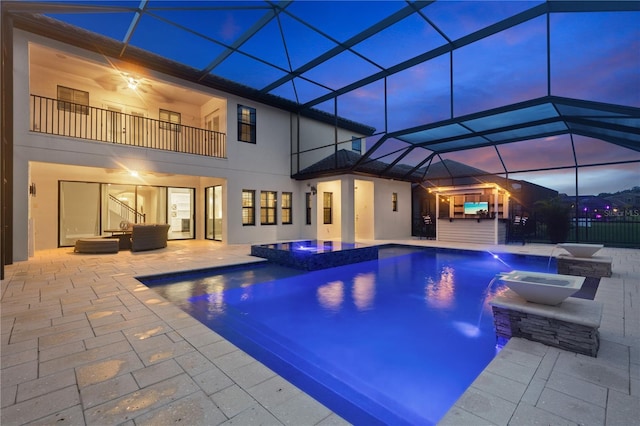 pool at dusk with pool water feature, a patio area, a lanai, and an in ground hot tub