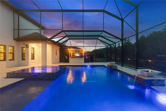 pool at dusk featuring an in ground hot tub, a patio, pool water feature, and glass enclosure