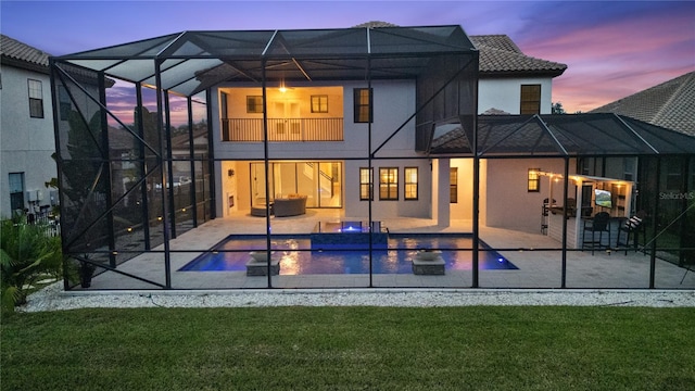 back house at dusk with a yard, glass enclosure, and a patio area