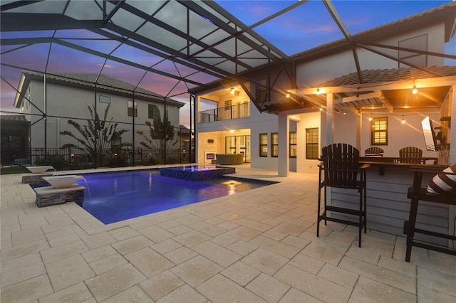 pool at dusk featuring an in ground hot tub, pool water feature, a patio, and exterior bar