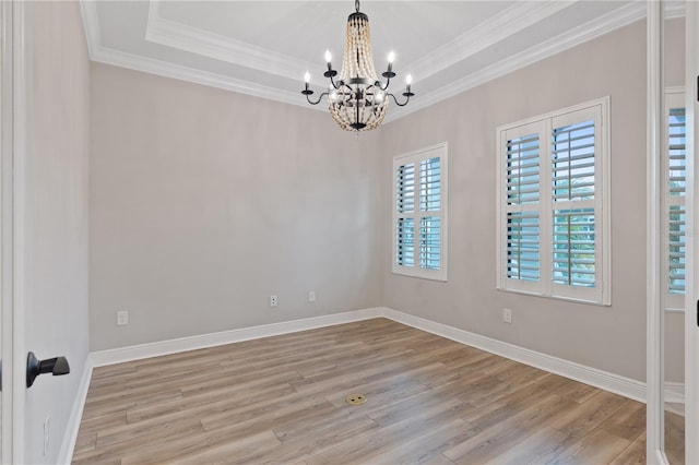 empty room featuring light hardwood / wood-style floors, crown molding, a tray ceiling, and a notable chandelier