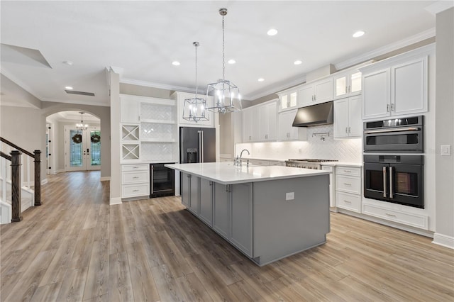 kitchen with white cabinetry, beverage cooler, hardwood / wood-style floors, an island with sink, and exhaust hood