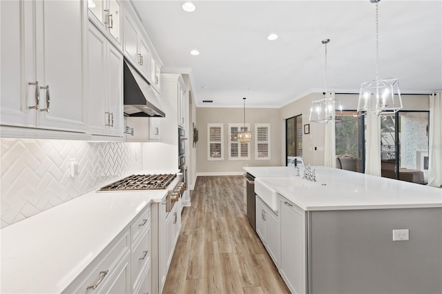 kitchen with a center island with sink, pendant lighting, light wood-type flooring, and white cabinetry