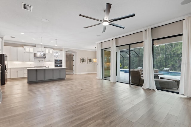 unfurnished living room featuring light wood-type flooring, ceiling fan, ornamental molding, and sink