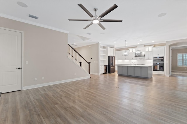 unfurnished living room with crown molding, ceiling fan, and light wood-type flooring