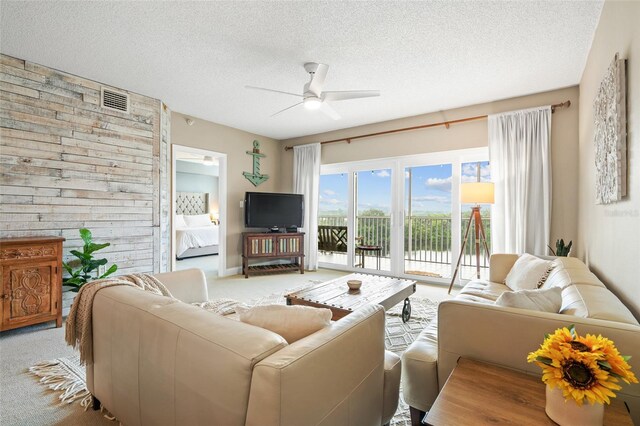 living room with a textured ceiling, light colored carpet, and ceiling fan