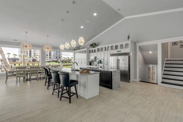 kitchen featuring pendant lighting, a notable chandelier, white cabinetry, an island with sink, and appliances with stainless steel finishes