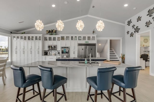 kitchen with stainless steel appliances, a kitchen breakfast bar, vaulted ceiling, and white cabinets