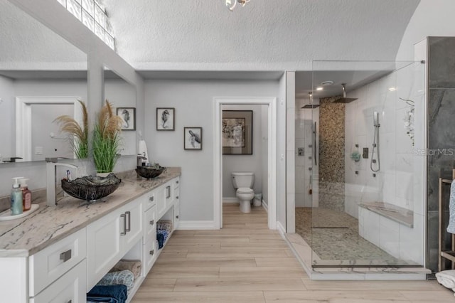 bathroom with a textured ceiling, vanity, hardwood / wood-style floors, a tile shower, and toilet