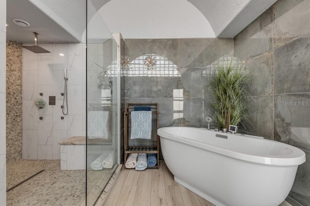 bathroom with tile walls, independent shower and bath, and a textured ceiling