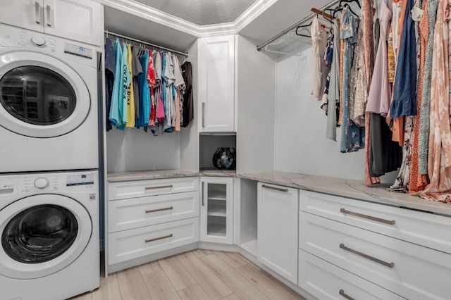 laundry room with cabinets, ornamental molding, stacked washer / dryer, and light wood-type flooring