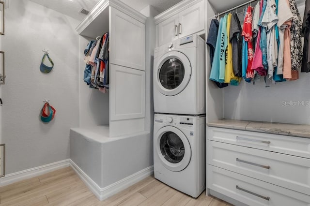 laundry area with stacked washing maching and dryer, light hardwood / wood-style floors, and cabinets