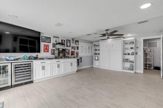 kitchen featuring beverage cooler, ceiling fan, white cabinetry, and a textured ceiling