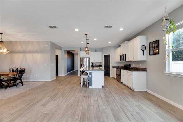 kitchen featuring pendant lighting, light hardwood / wood-style flooring, a kitchen island with sink, stainless steel appliances, and sink