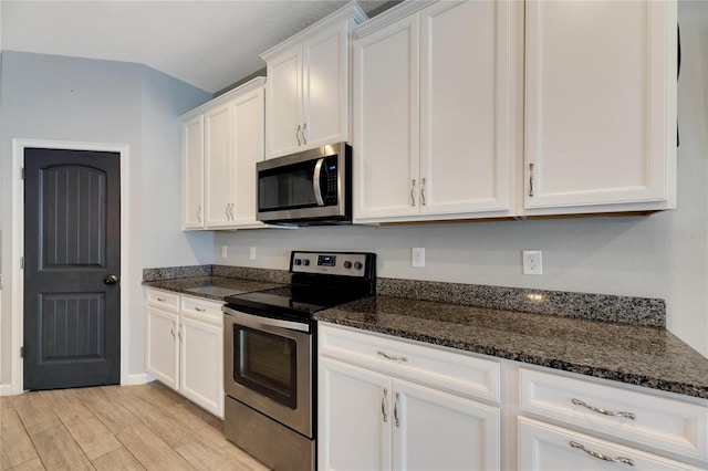 kitchen with dark stone counters, white cabinetry, light hardwood / wood-style flooring, and stainless steel appliances