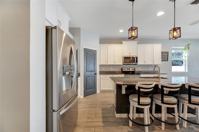 kitchen with white cabinets, stainless steel appliances, light hardwood / wood-style floors, sink, and a breakfast bar