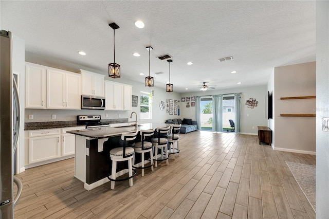 kitchen with a center island with sink, appliances with stainless steel finishes, ceiling fan, light wood-type flooring, and white cabinets