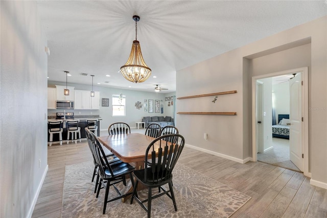 dining area with ceiling fan with notable chandelier and light wood-type flooring