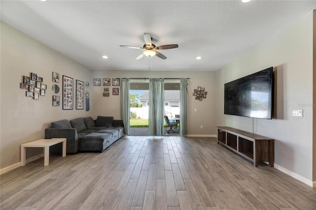 living room featuring light wood-type flooring, a textured ceiling, and ceiling fan