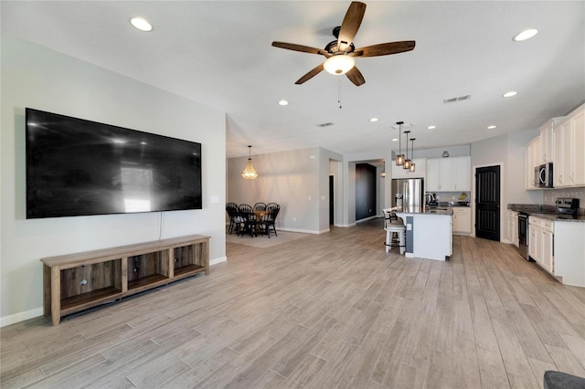 kitchen with appliances with stainless steel finishes, an island with sink, ceiling fan, and pendant lighting