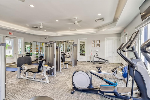 exercise room featuring a tray ceiling, ceiling fan, and light colored carpet