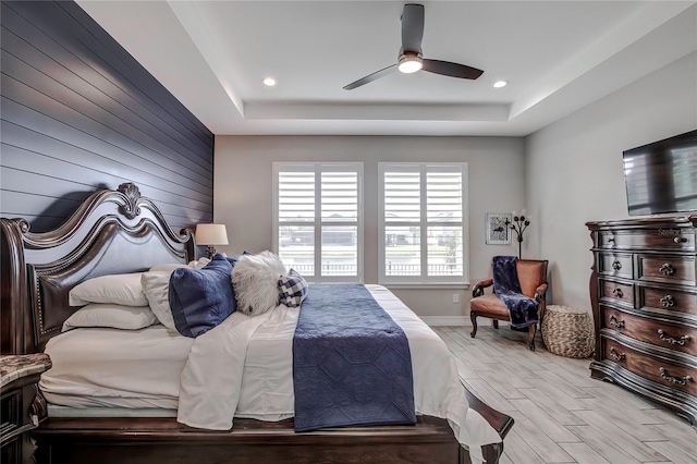 bedroom with ceiling fan, light hardwood / wood-style floors, and a raised ceiling