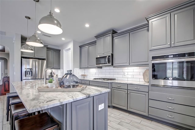 kitchen with a breakfast bar, gray cabinets, stainless steel appliances, and hanging light fixtures