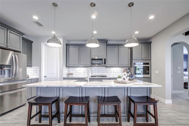 kitchen with pendant lighting, backsplash, a kitchen island with sink, and appliances with stainless steel finishes