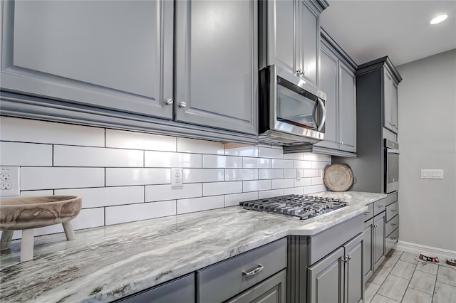 kitchen with decorative backsplash, stainless steel appliances, gray cabinets, and light stone counters