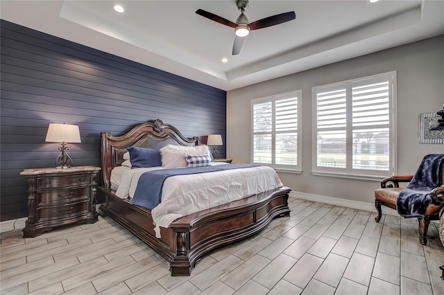 bedroom with light wood-type flooring, a tray ceiling, and ceiling fan