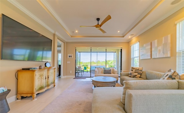 living room with ornamental molding, a raised ceiling, light hardwood / wood-style flooring, and ceiling fan