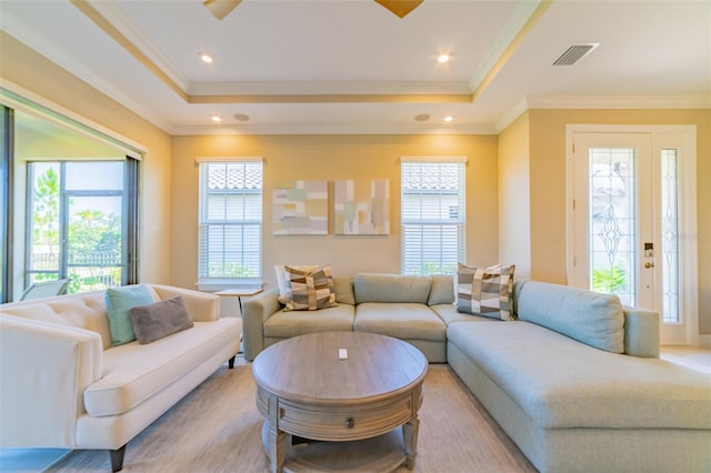 living room with crown molding, a tray ceiling, and light hardwood / wood-style floors