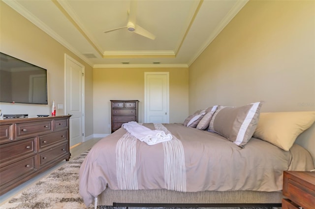 bedroom featuring a tray ceiling, ceiling fan, crown molding, and light hardwood / wood-style flooring