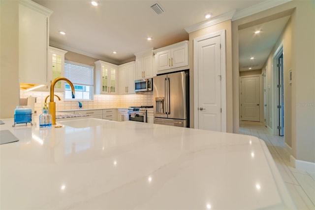 kitchen with ornamental molding, tasteful backsplash, stainless steel appliances, and white cabinets