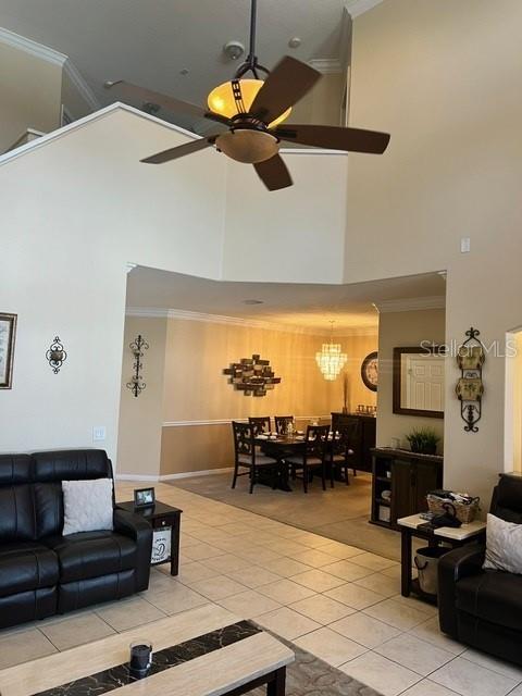 tiled living room with ornamental molding, a towering ceiling, and ceiling fan with notable chandelier