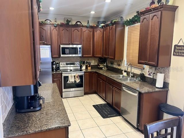 kitchen featuring ornamental molding, light tile patterned floors, sink, decorative backsplash, and appliances with stainless steel finishes