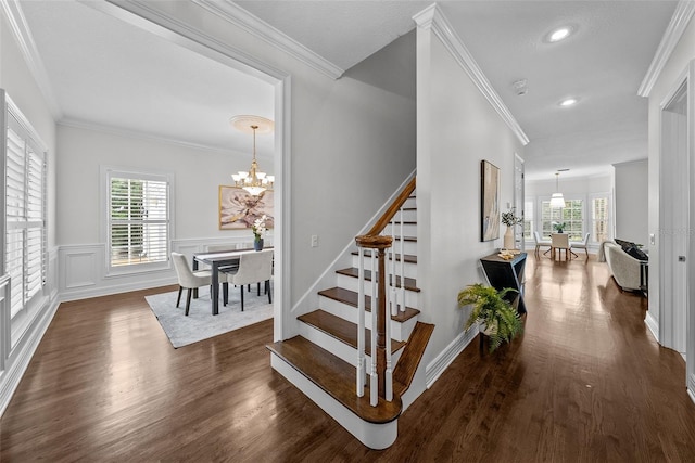 stairway featuring hardwood / wood-style floors, ornamental molding, a wealth of natural light, and a chandelier