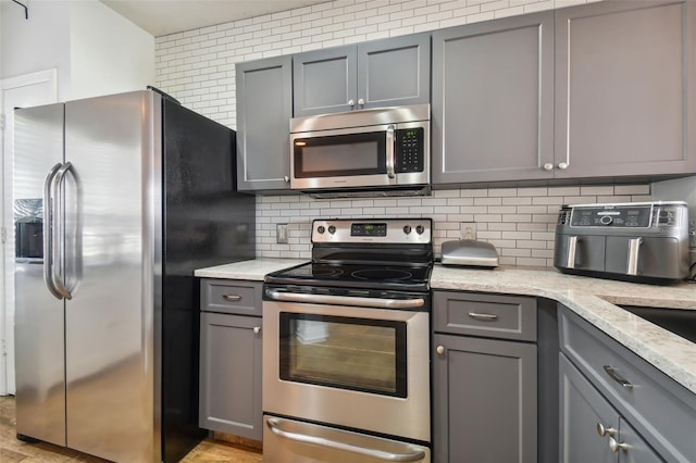 kitchen with light stone countertops, gray cabinets, appliances with stainless steel finishes, and backsplash