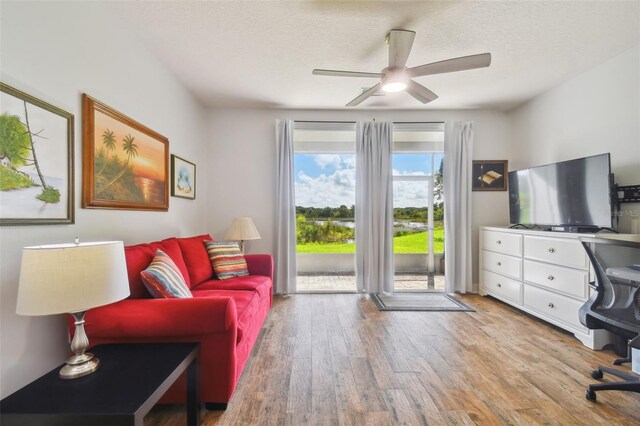 living room featuring light hardwood / wood-style flooring, ceiling fan, and a textured ceiling