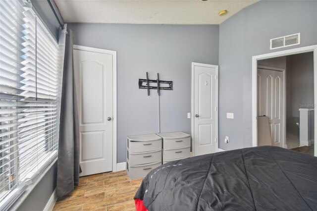 bedroom featuring a textured ceiling, vaulted ceiling, and light hardwood / wood-style flooring