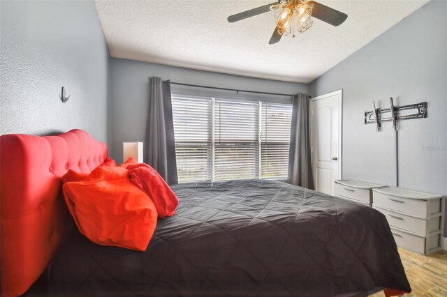 bedroom with a textured ceiling, light hardwood / wood-style floors, vaulted ceiling, and ceiling fan