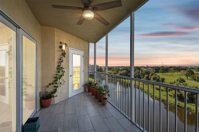 balcony at dusk featuring a water view and ceiling fan